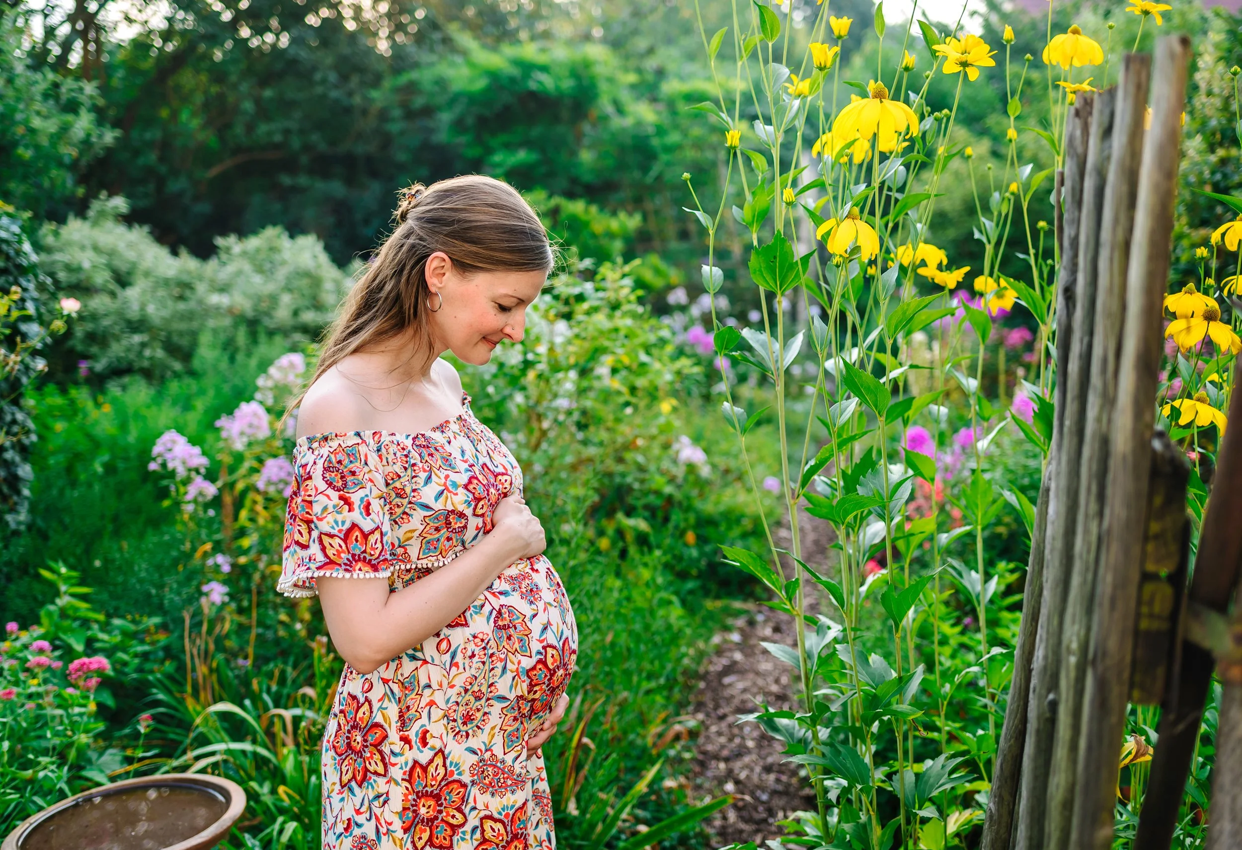 Schwangere Frau in einem gemusterten Kleid bei einem Babybauch Shooting im Garten.
