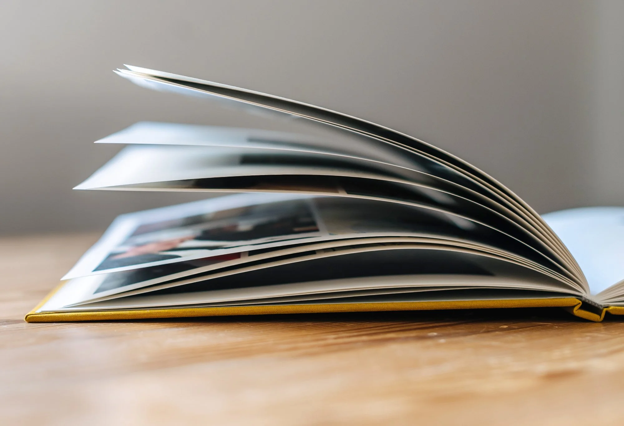 Ein Fotobuch mit gelbem Leineinband liegt aufgeschlagen auf einem Holztisch