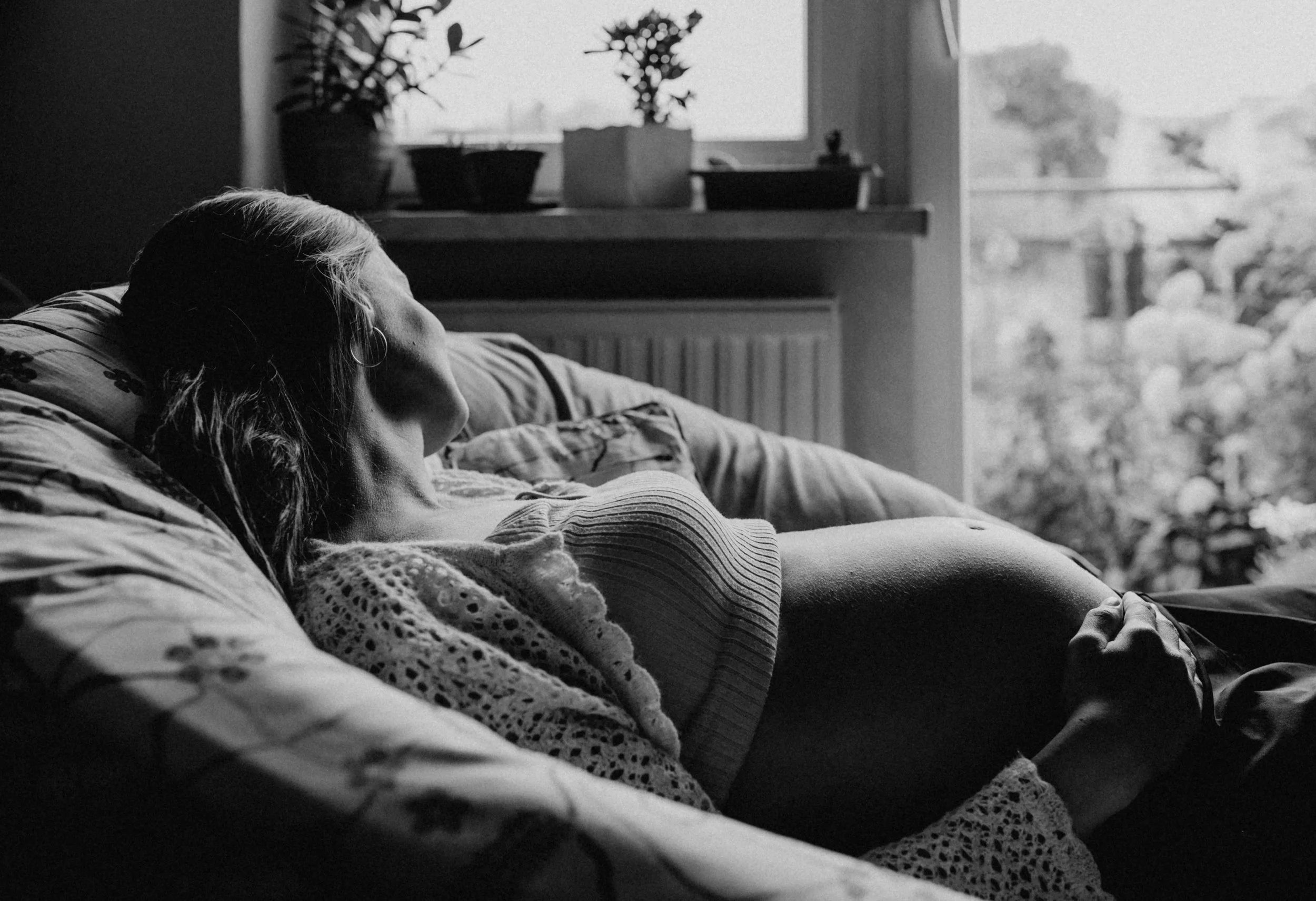 Babybauch Foto einer schwangeren Frau unter einem großen Fenster mit weichem Tageslicht.