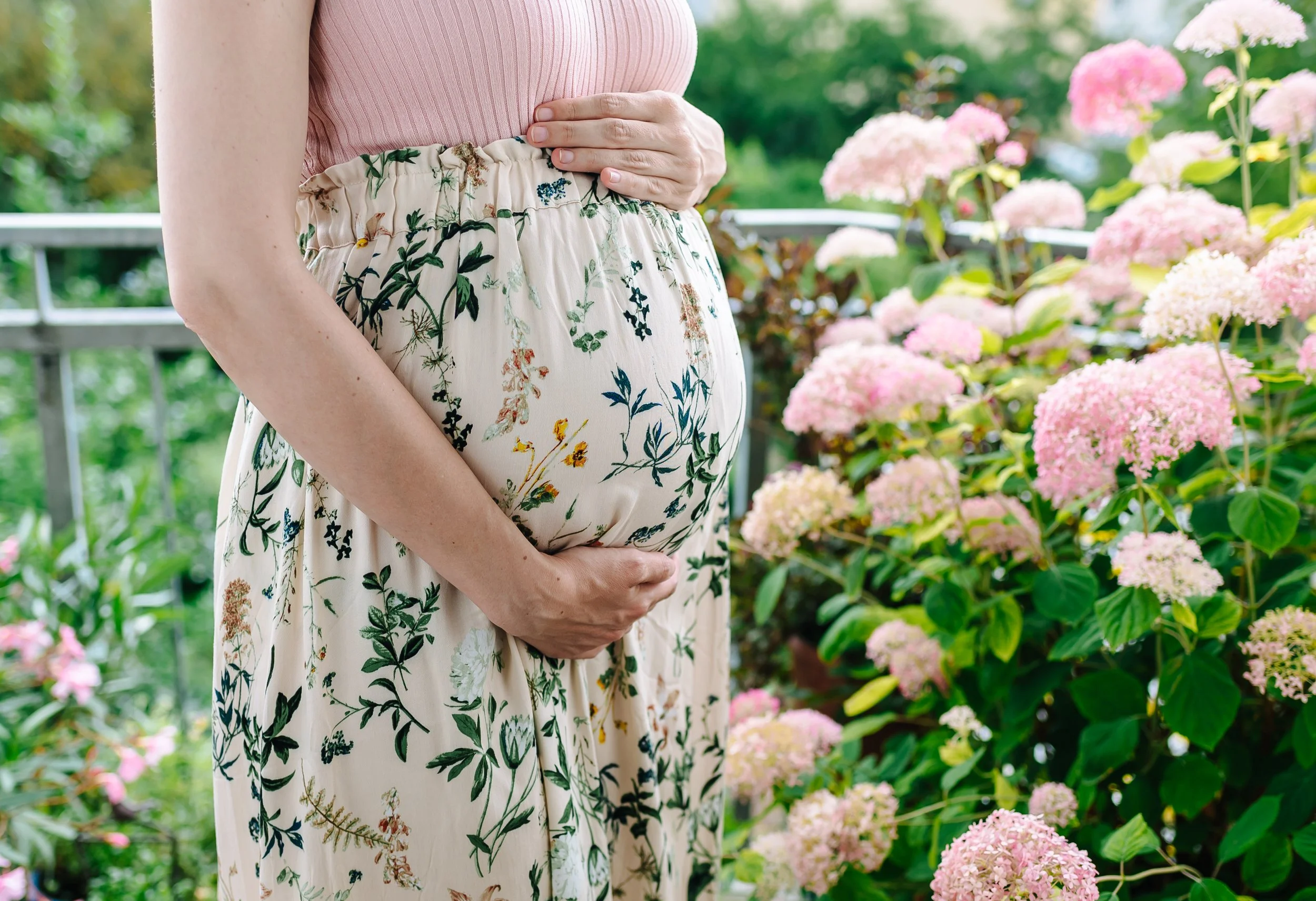 Babybauch Foto einer schwangeren Frau im Kleid mit den Händen auf dem Bauch.