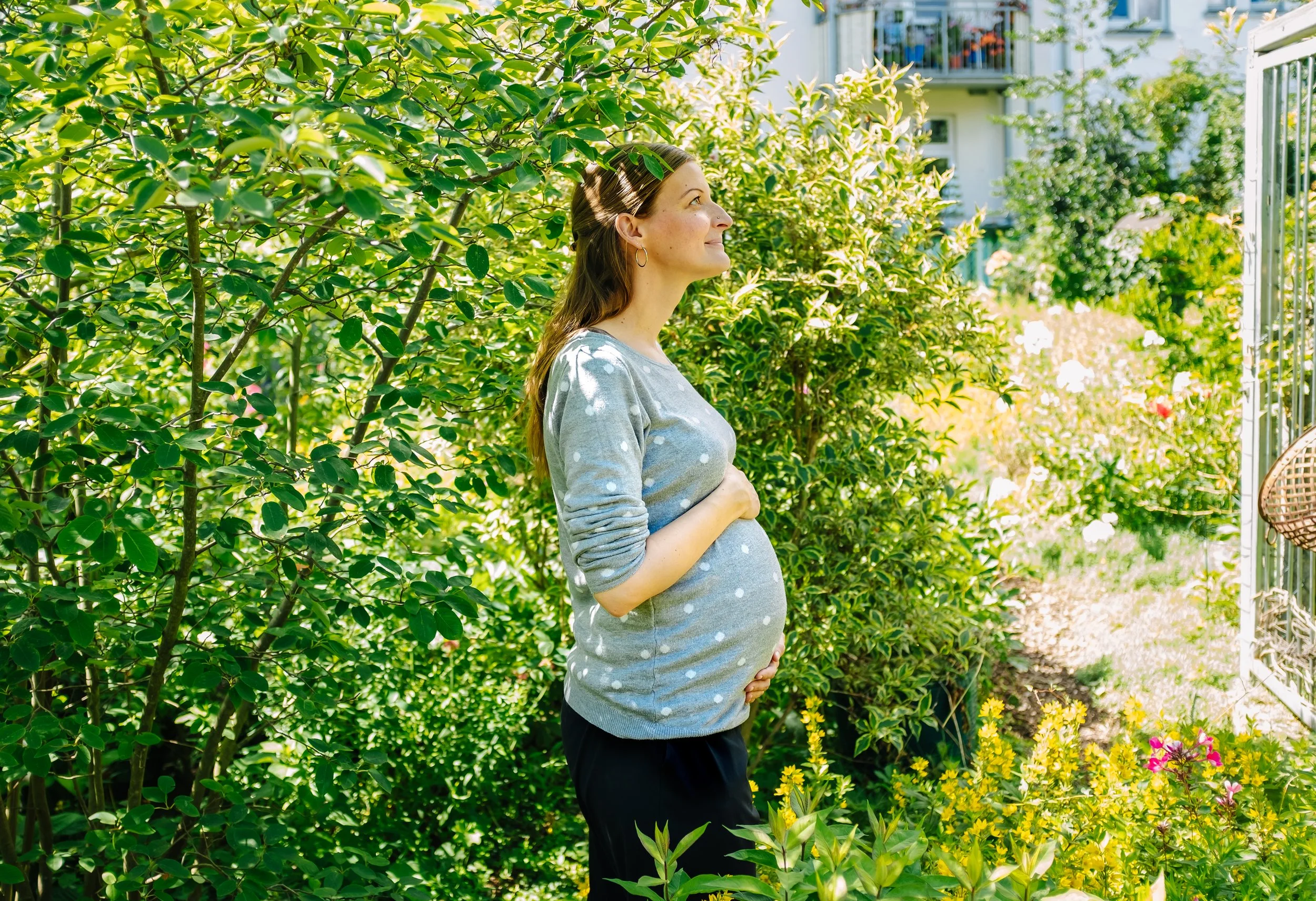 Schwangere Frau blickt bei einem Babybauch Foto nach oben in einen Garten.