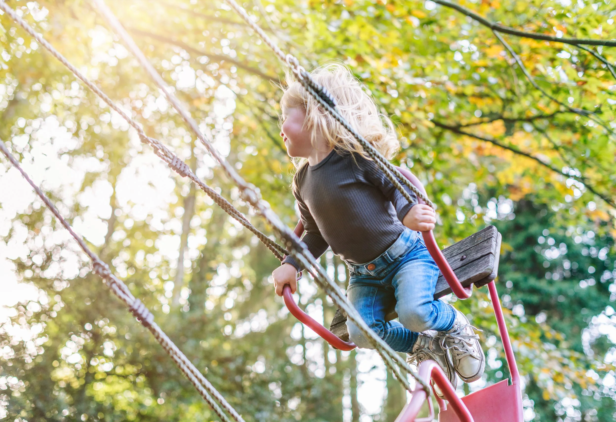 Kind schaukelt auf dem Spielplatz und wird natürlich ohne Posieren fotografiert.