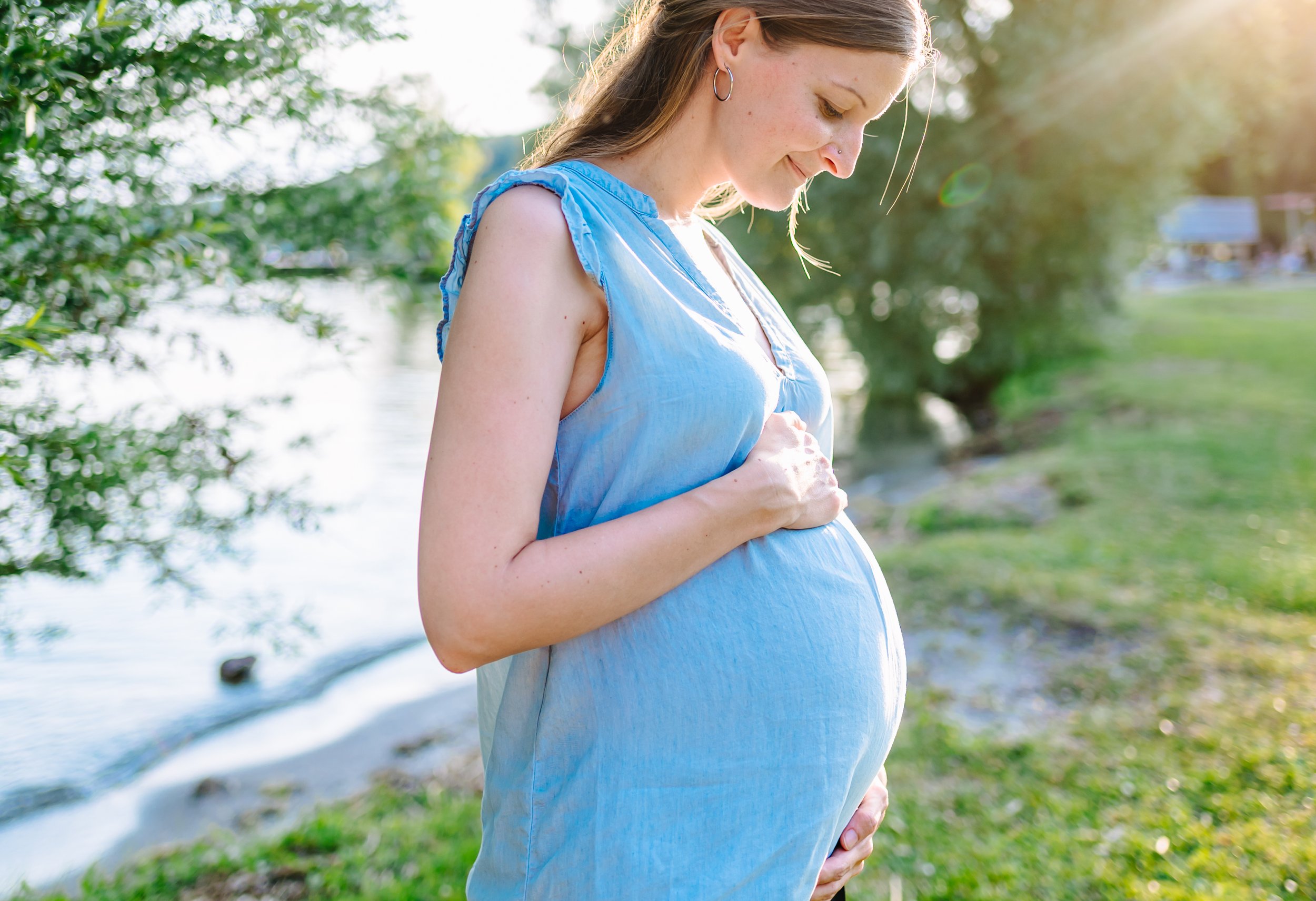 Schwangere Frau bei einem Babybauch Shooting am See kurz vor Sonnenuntergang.