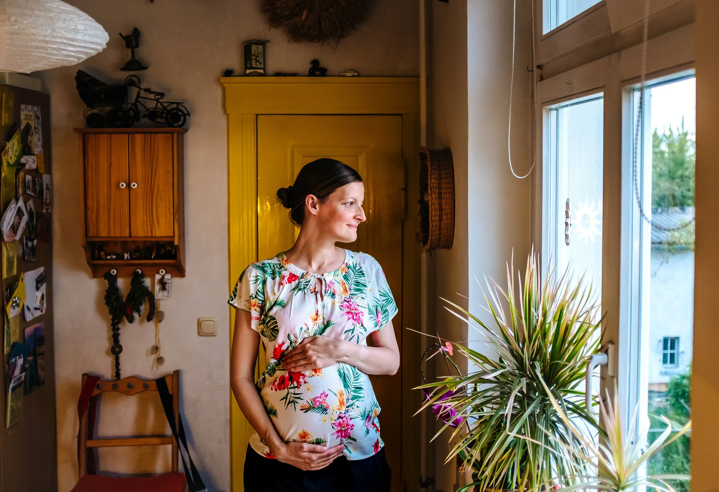 Babybauch Foto am Fenster in einer Küche. Selbstporträt einer schwangeren Frau mit 35 mm Objektiv.
