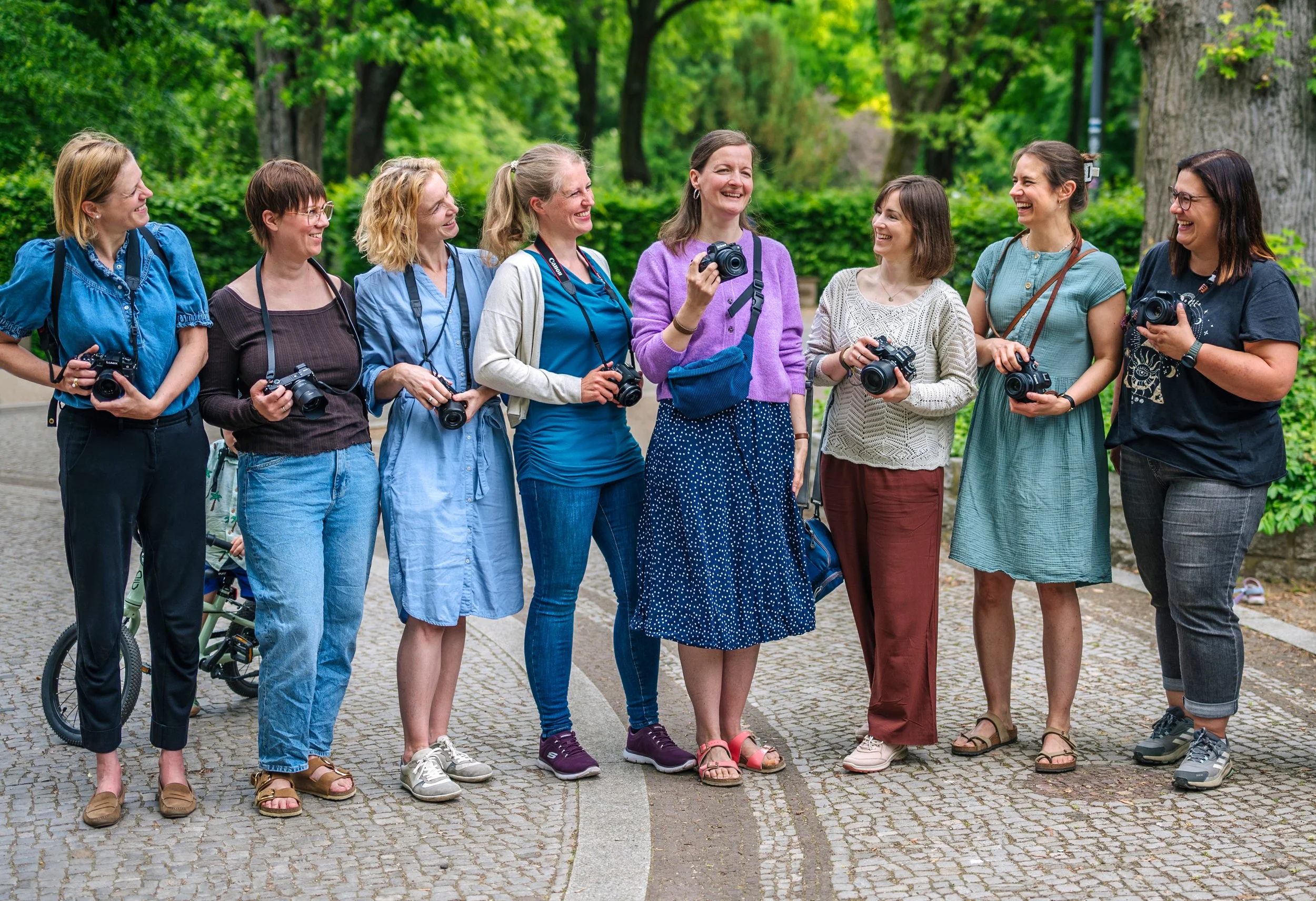 Mamas mit Kameras stehen nebeneinander und lachen.