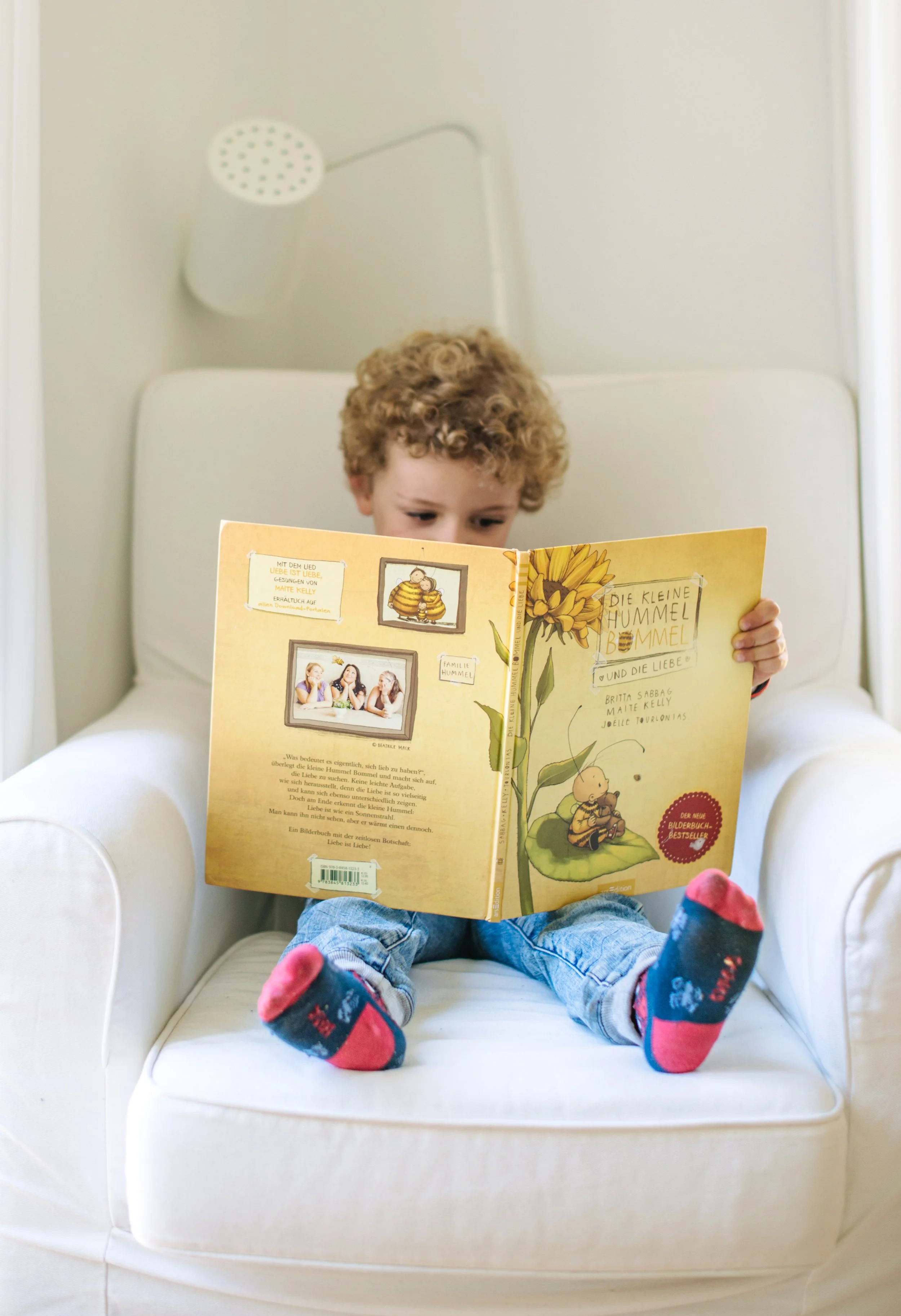 Ein kleiner Junge sitzt auf einem weißen Sessel und liest das Kinderbuch Die kleine Hummel Bommel.