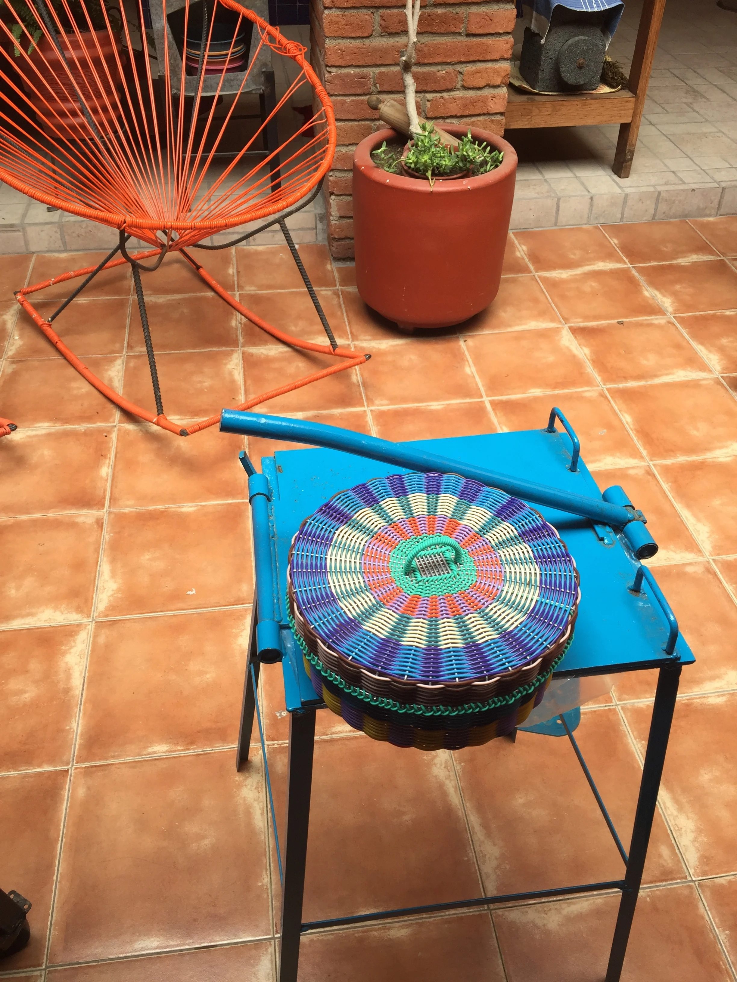 A traditional tortilla press and colorful woven basket for keeping them warm.