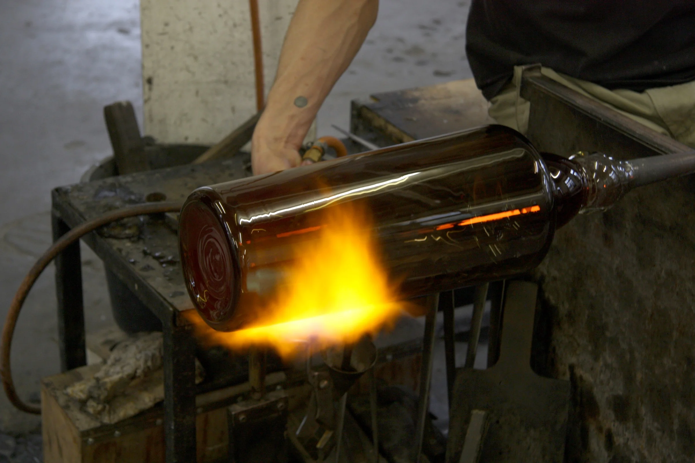  Using fire and his agility to work the molten glass, he stretches out a part of the form, evolving it from a primitive to functional object, as this part will house the light fixture. 