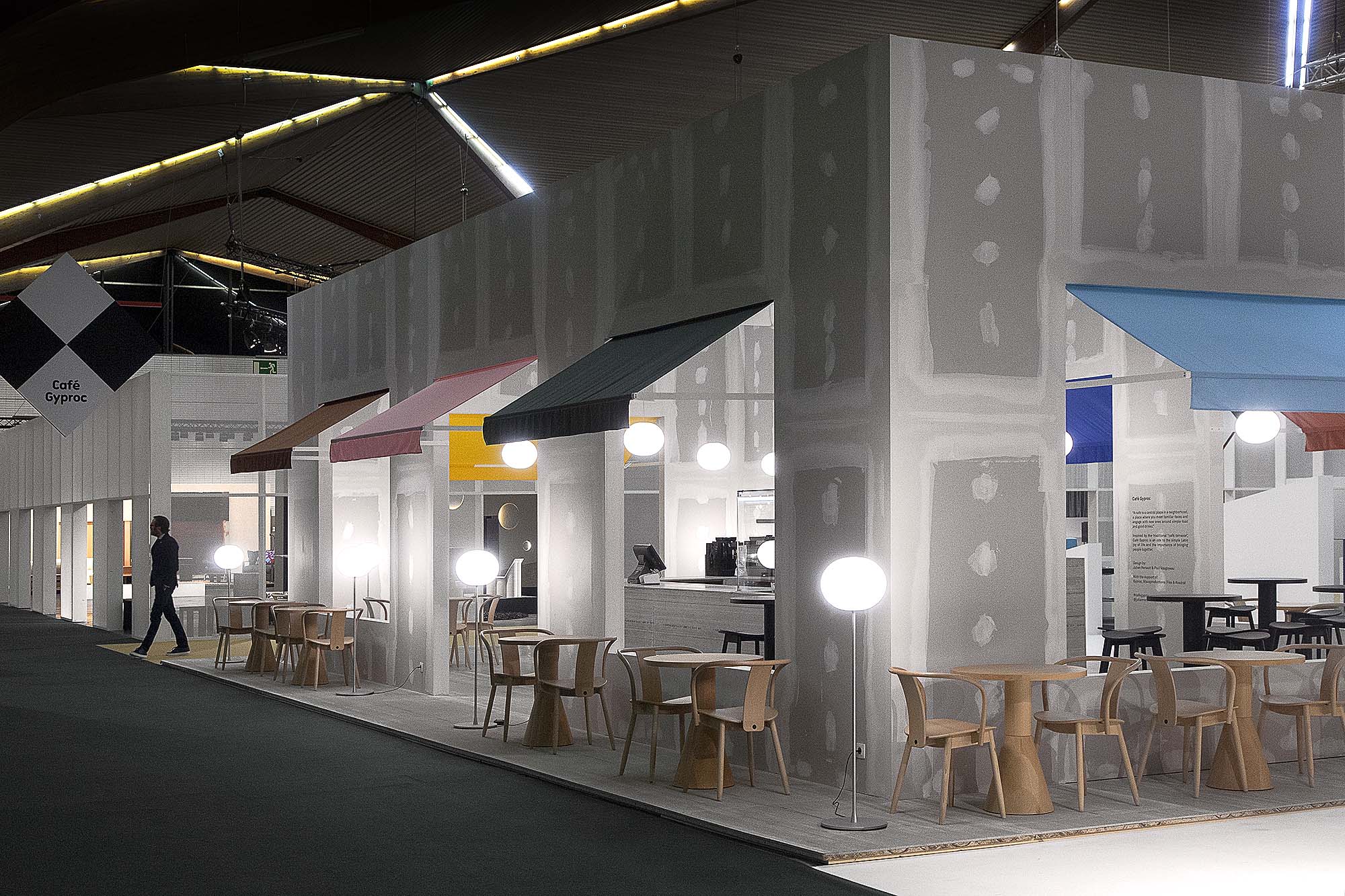 The architecture of Café Gyproc is envisioned as an archetype of the communal place. The large regular window openings, the colorful sun-blinds, the center bar, and bistro chairs facing the streets will immediately tell the wanderer what this place is about.