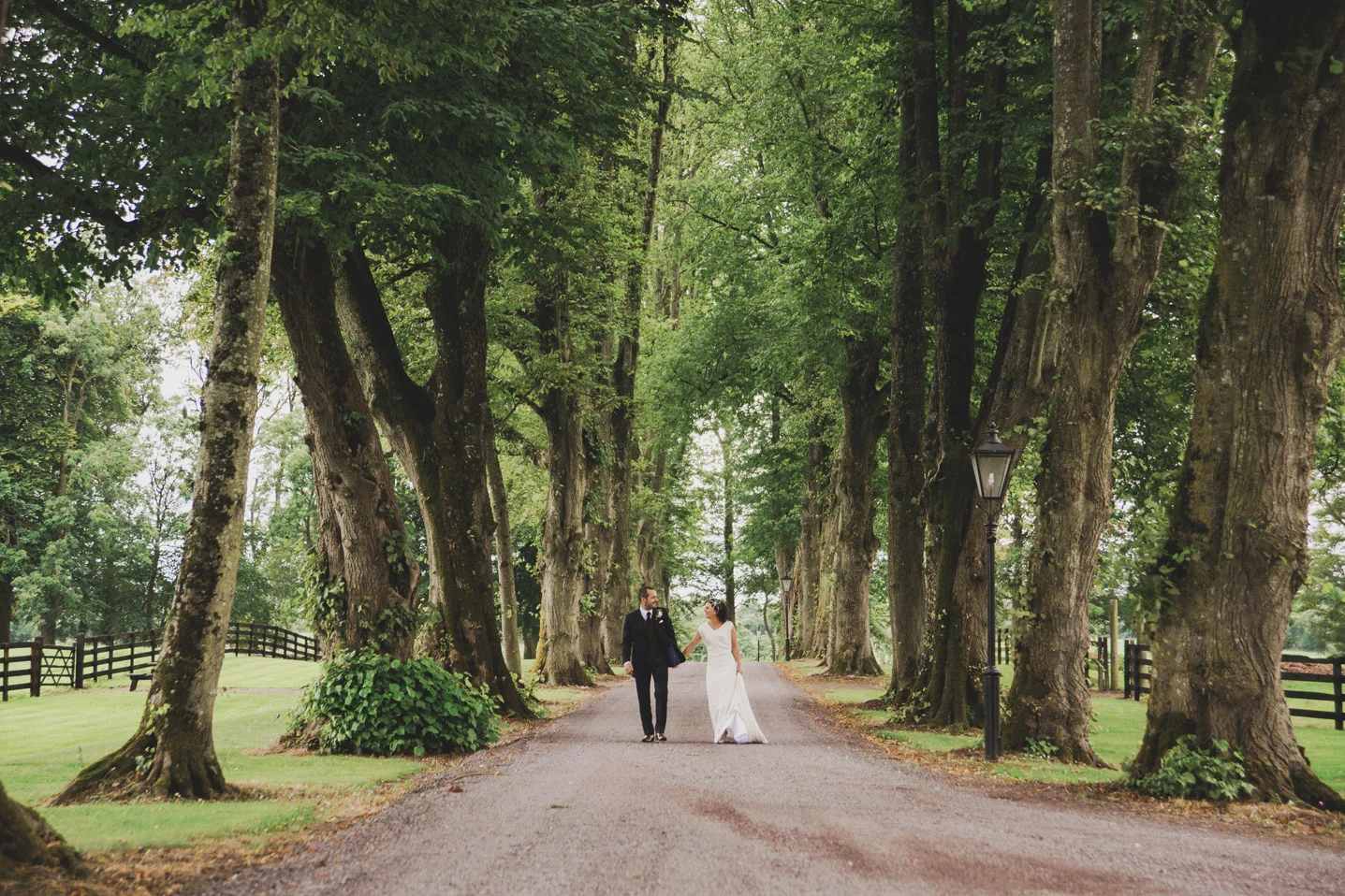 Bride and groom walking down a tree-lined avenue in Tankardstown House Meath Wedding photographers meath ireland