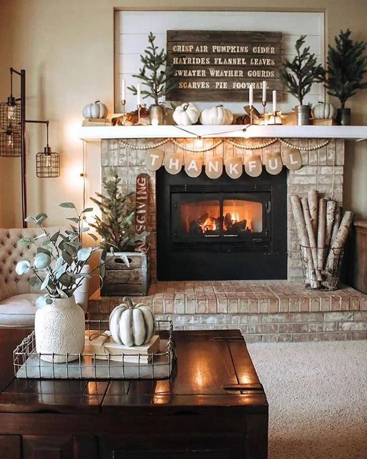 Rustic farmhouse fall fireplace with a wood word sign, mini evergreen trees, white pumpkins, wood bead garland, and a Thankful banner on a brick fireplace