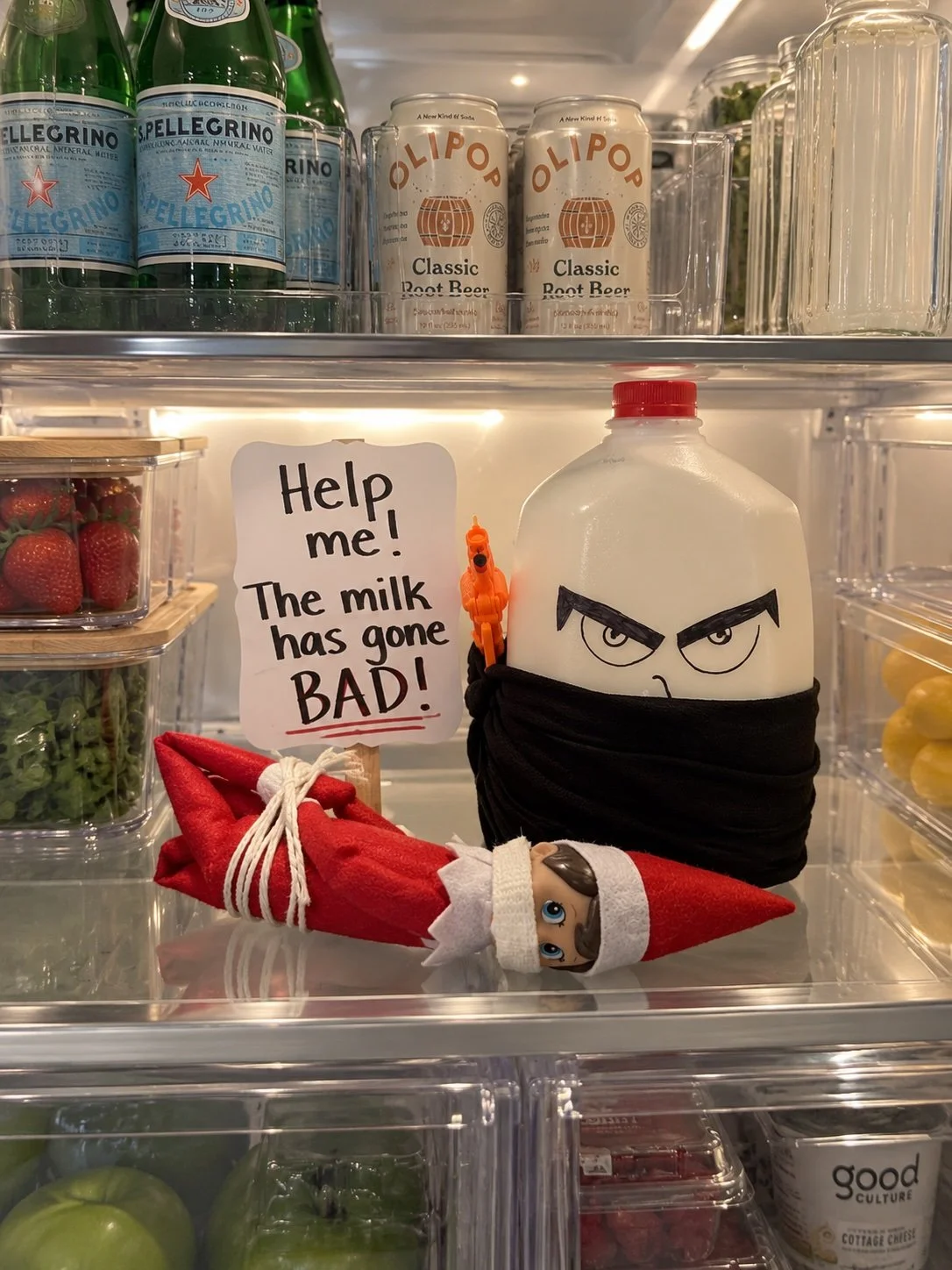 Elf on the Shelf next to a milk jug with a mischievous face drawn on it