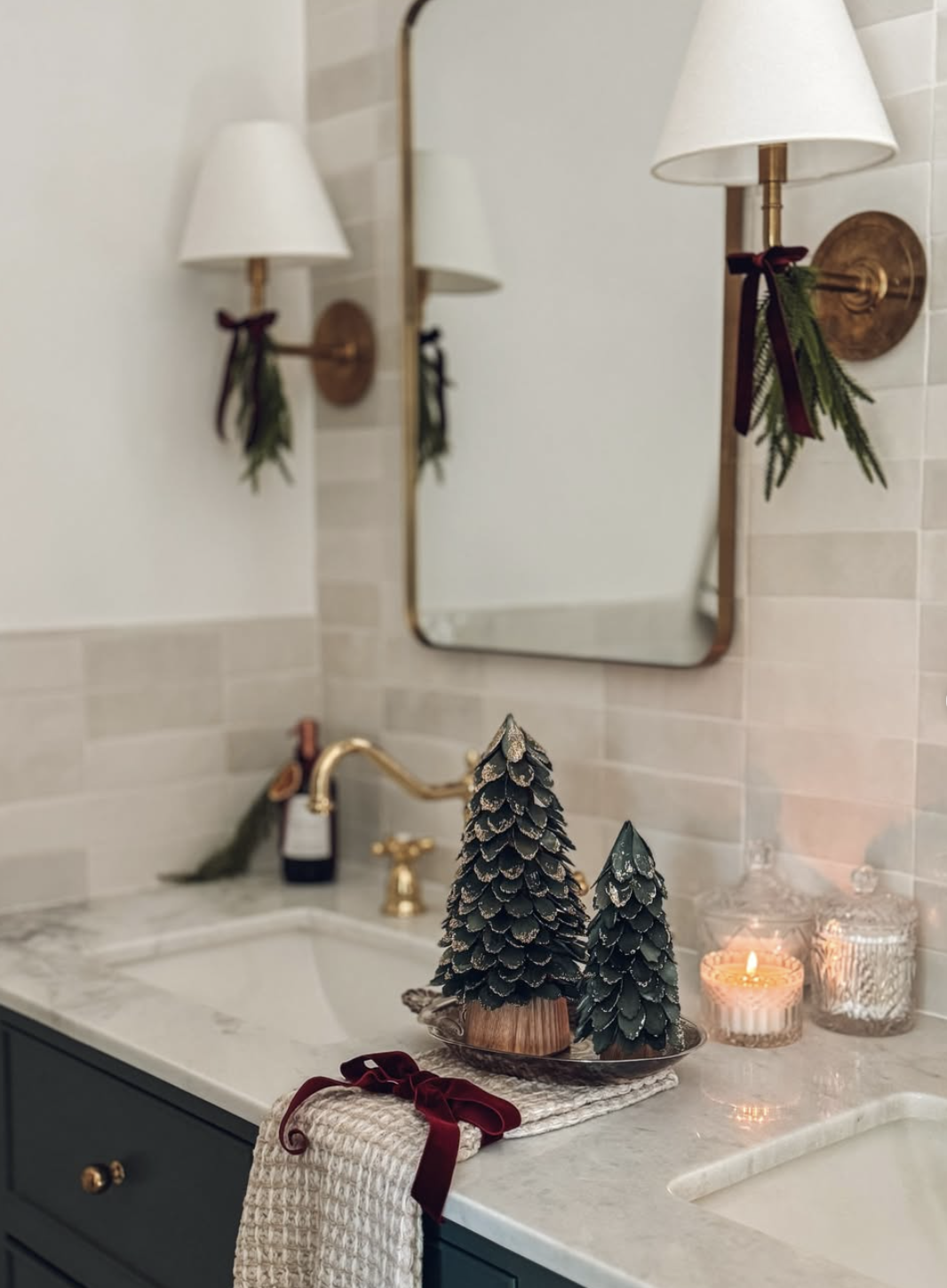 Christmas bathroom with brass wall sconces tied with cedar sprigs and burgundy velvet bows