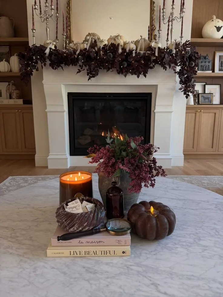 Elegant fall fireplace with silver candelabras holding plum taper candles, cream pumpkins tied with ribbon bows, and a dark plum leaf garland with fairy lights