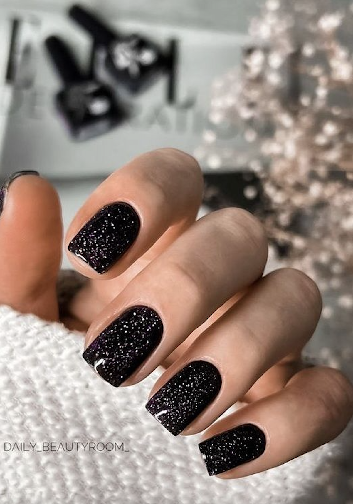 Short nails painted in black holographic glitter polish for a festive holiday look