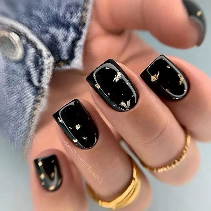Short black nails with scattered gold foil flakes near the cuticles