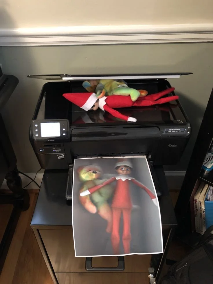 Elf on the Shelf on a copy machine surrounded by printed copies of himself