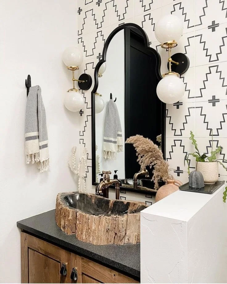 Boho western bathroom vanity with petrified wood vessel sink, black arched mirror, brass globe sconces, and Aztec tile