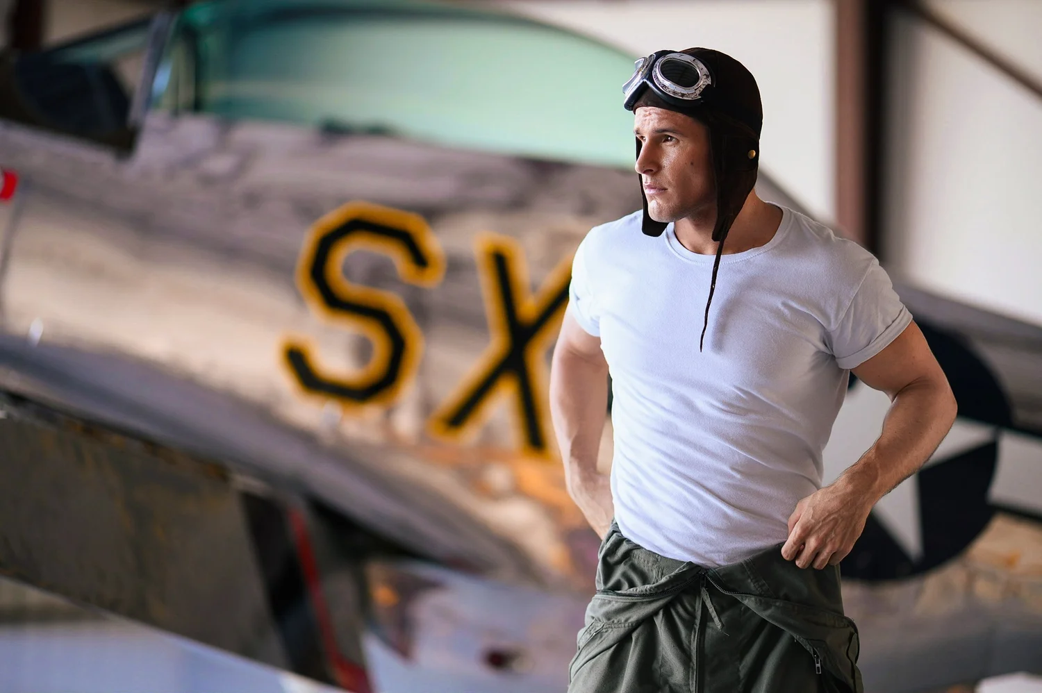 Man in a leather aviator cap and goggles beside a vintage airplane