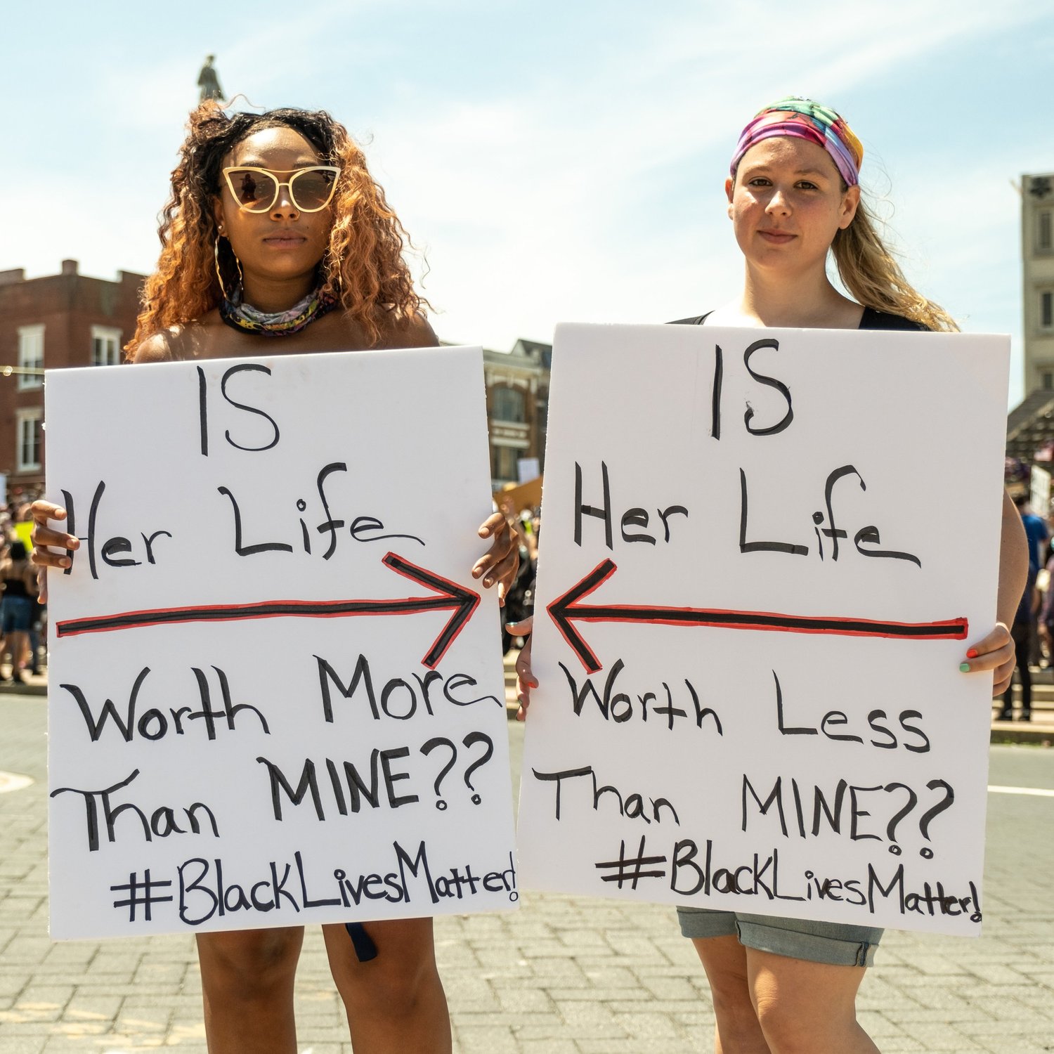 Two young women holding signs asking “Is her life worth more than mine?” and “Is her life worth less than mine?”