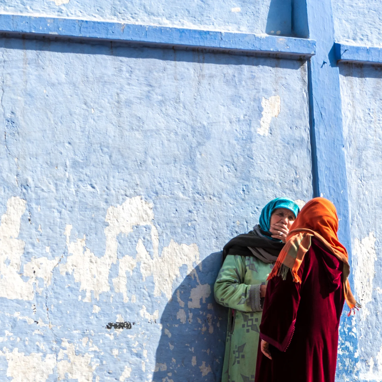 Two women in bright headscarves against a vivid blue wall