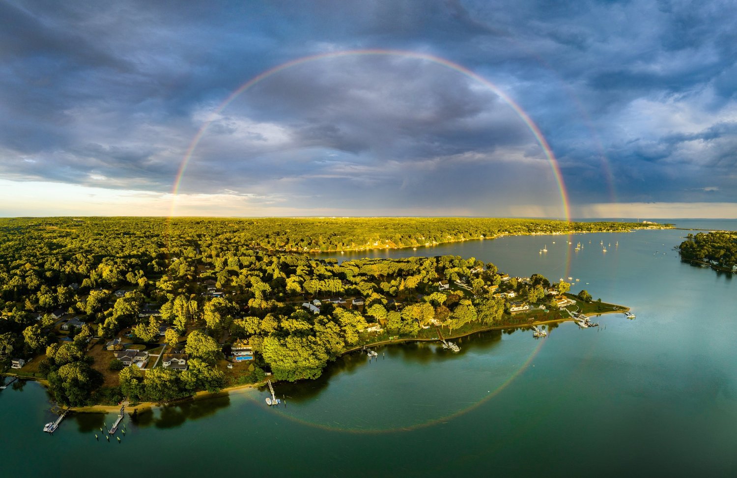 Aerial view of a lake shore beneath a circular rainbow