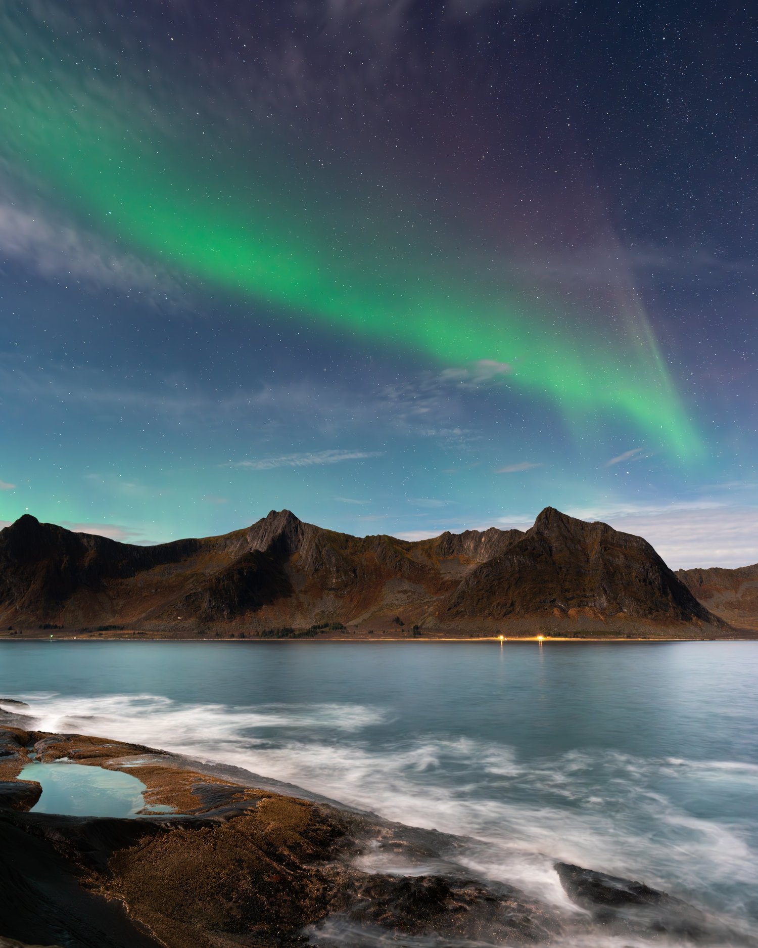 Green aurora over mountains and a rocky shoreline at night