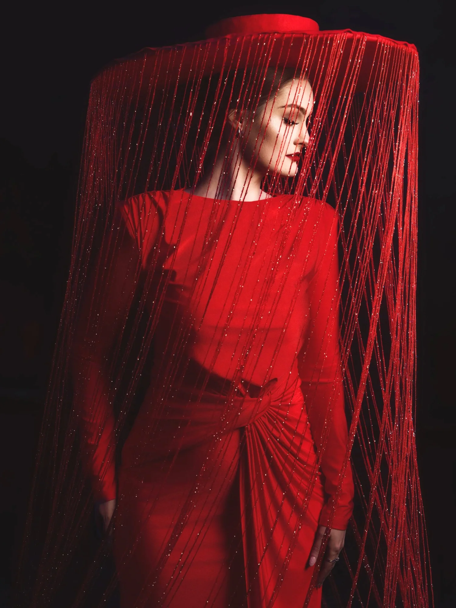 Woman dressed in red under a red fringed hat against a dark background