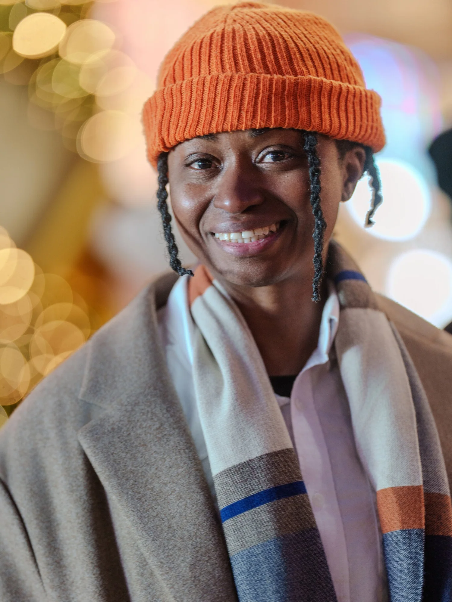Participant in an orange beanie smiling against golden holiday lights