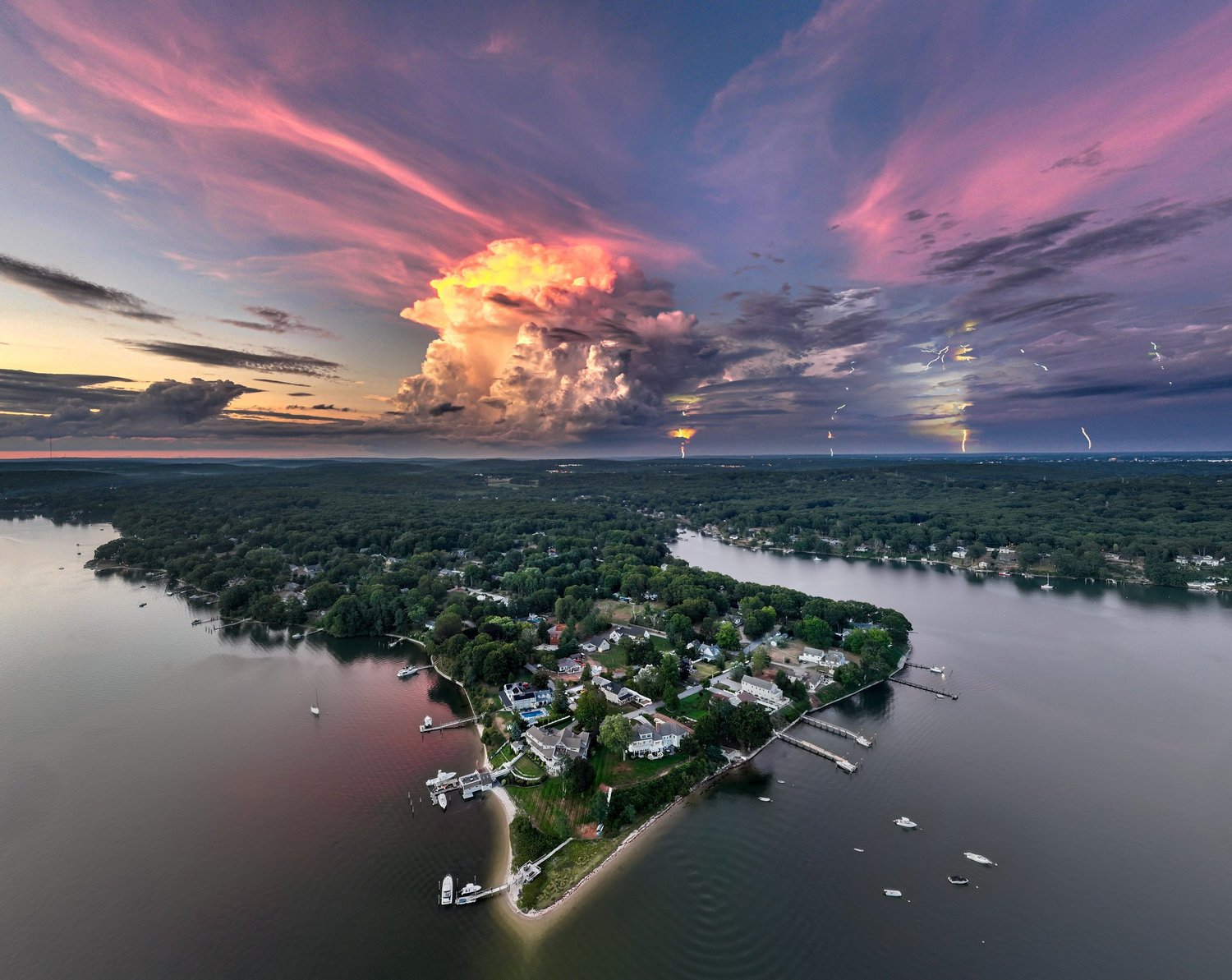 Aerial view of a wooded peninsula under pink and orange sunset clouds