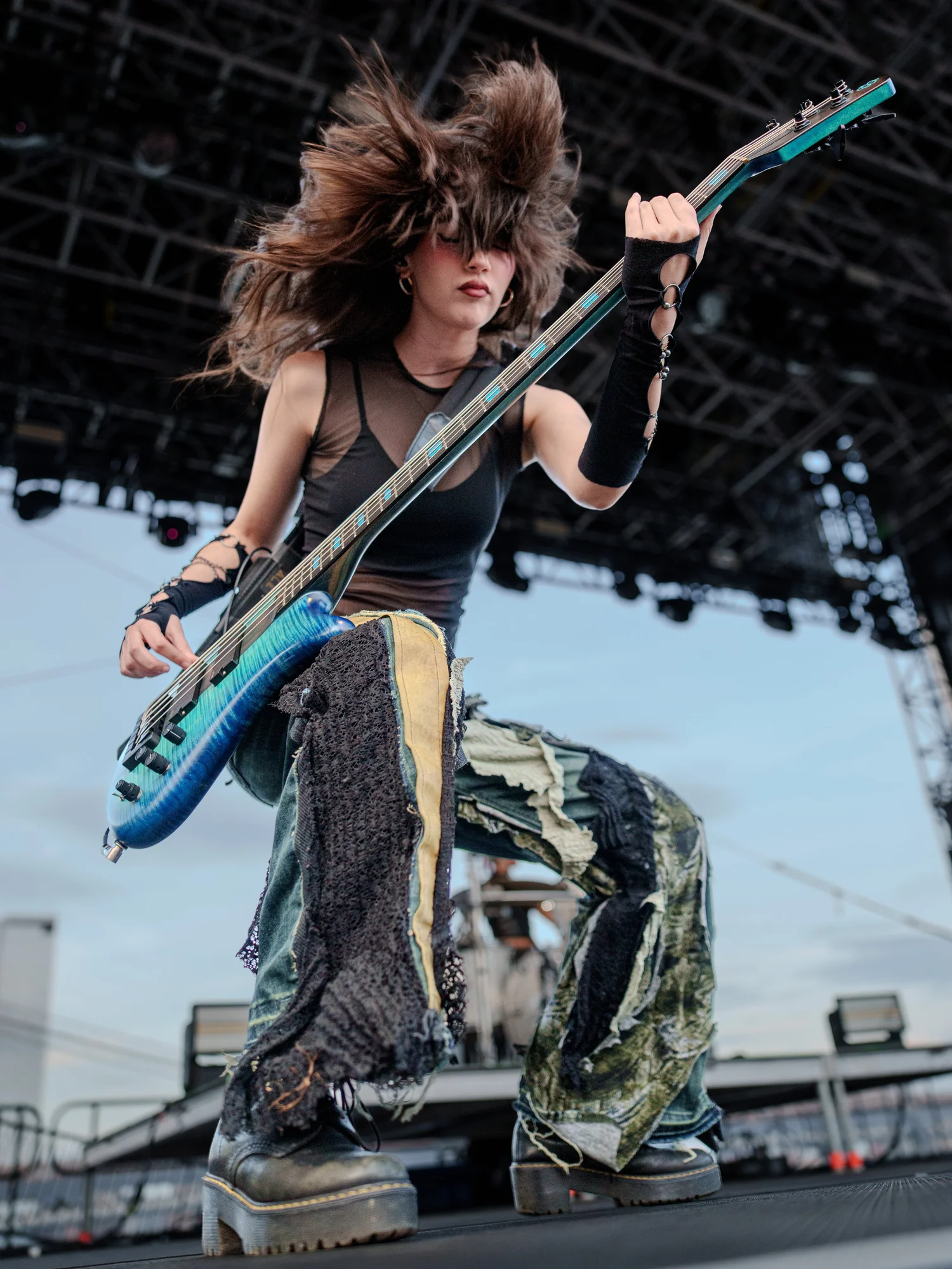 Woman with windswept hair playing a blue bass guitar on an outdoor stage