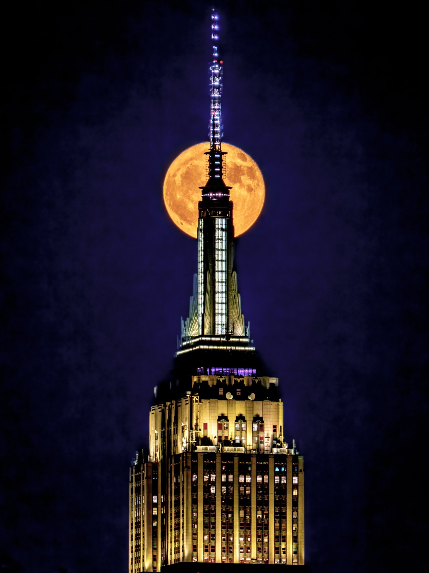 The Empire State Building’s lit spire in front of the full moon