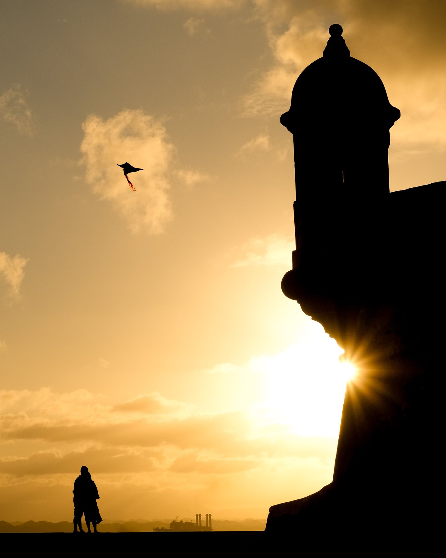 Silhouette of a stone sentry box against the sunset, a bird overhead and a person below