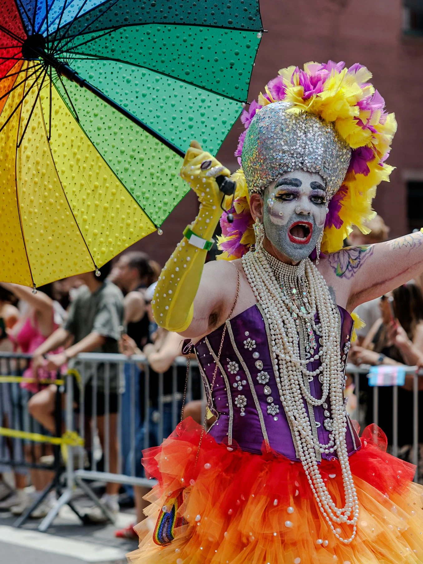 Drag performer in a ruffled rainbow costume under a rainbow umbrella
