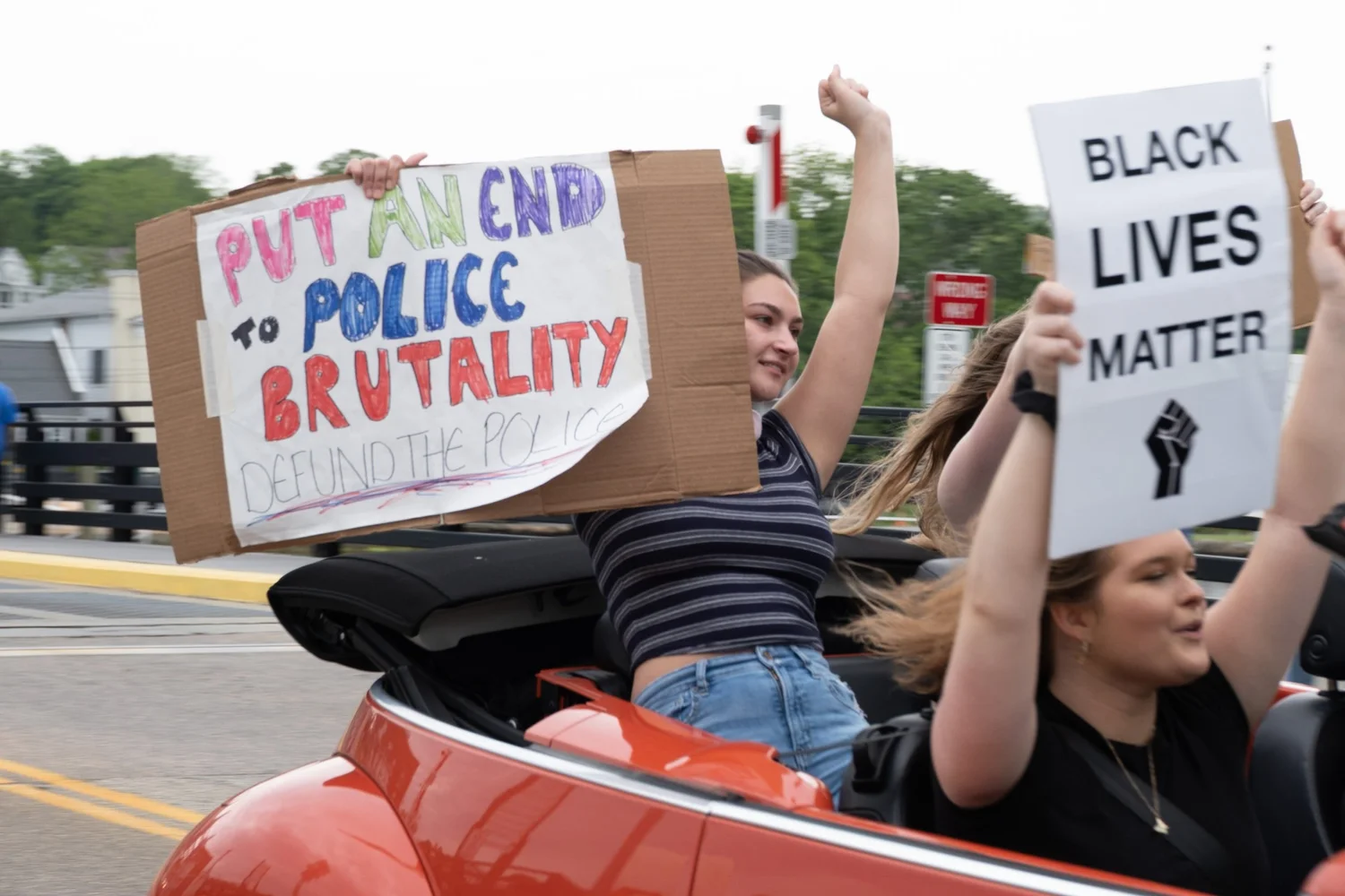 Protesters in a convertible holding signs reading “Put an end to police brutality” and “Black lives matter”