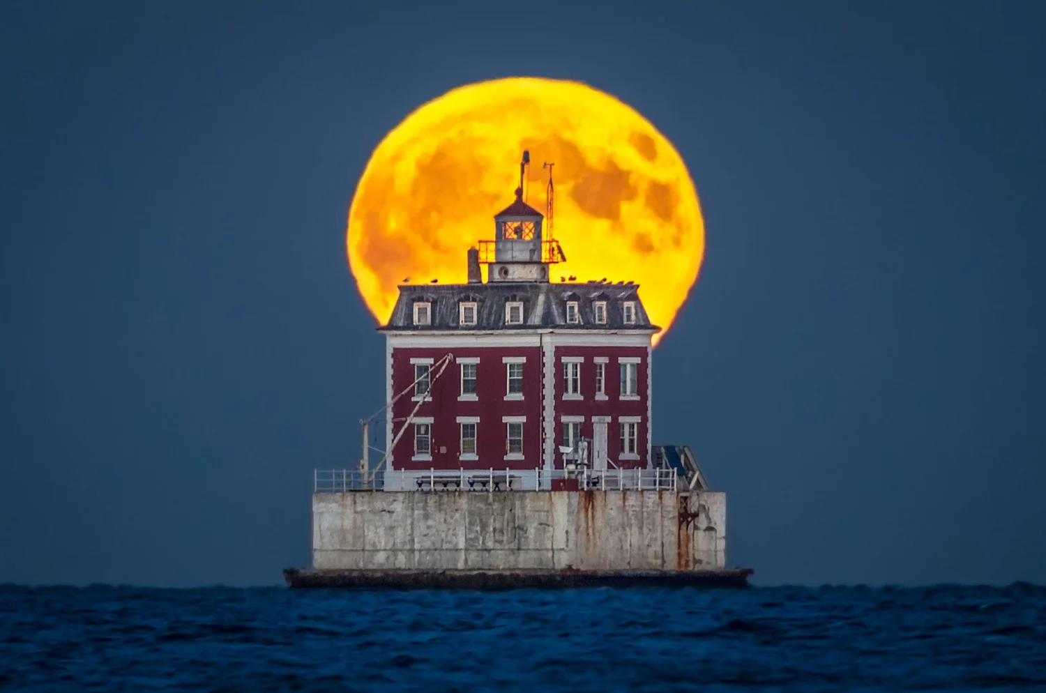 Full moon rising directly behind a brick lighthouse standing in the sea