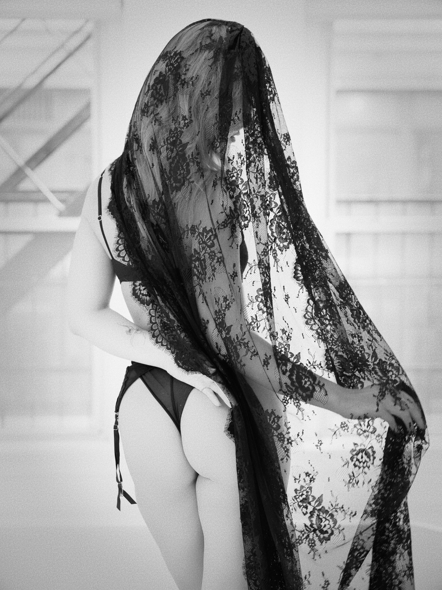 Model seen from behind, draped from head to hip in black lace, in soft window light