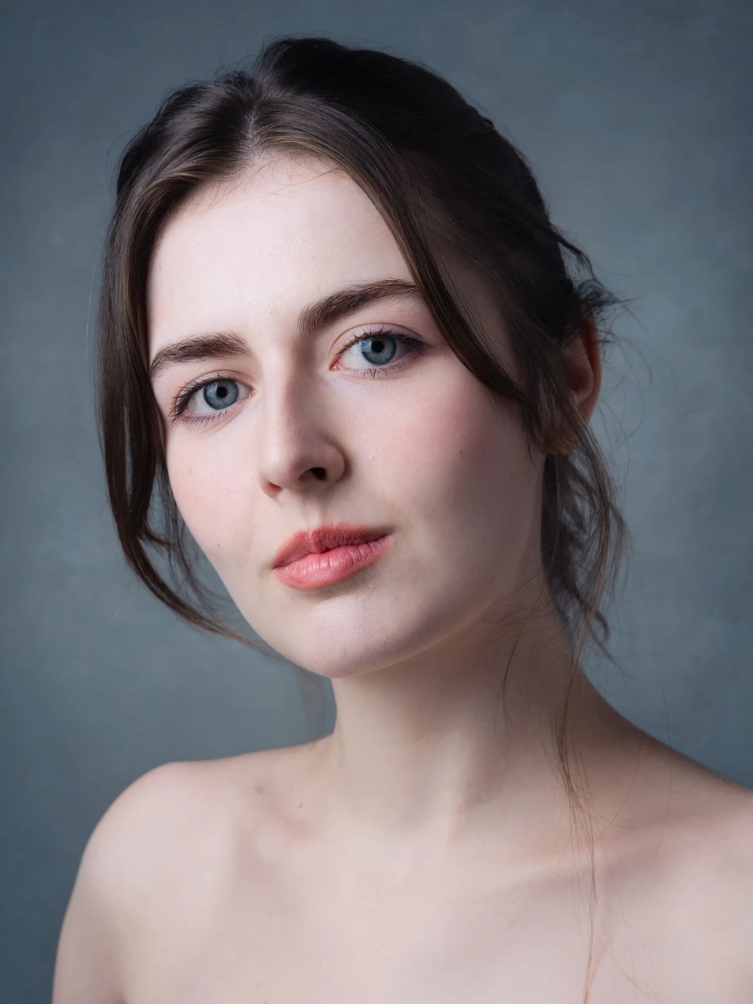 Woman with dark hair pulled back in soft, painterly light against a blue-gray backdrop