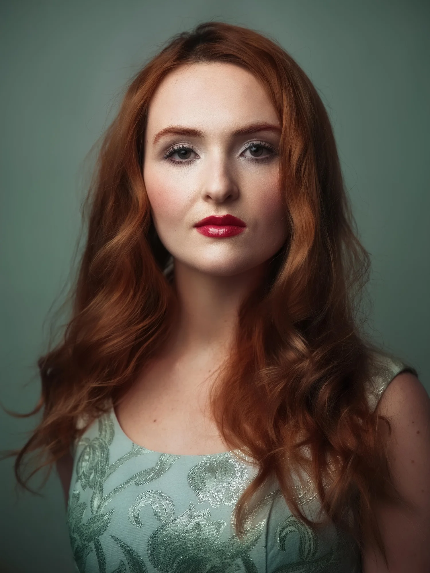 Red-haired woman in a pale green lace dress against a muted green backdrop