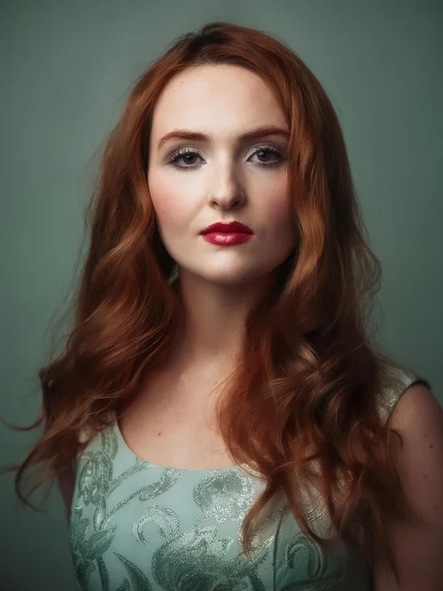 Red-haired woman in a pale green lace dress against a muted green backdrop