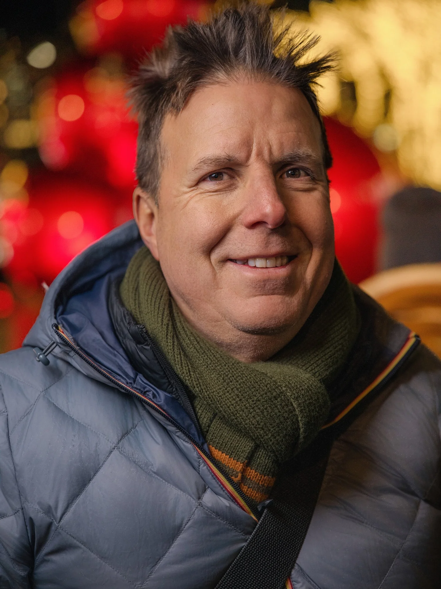 Smiling participant in a gray puffer and olive scarf among giant red ornaments