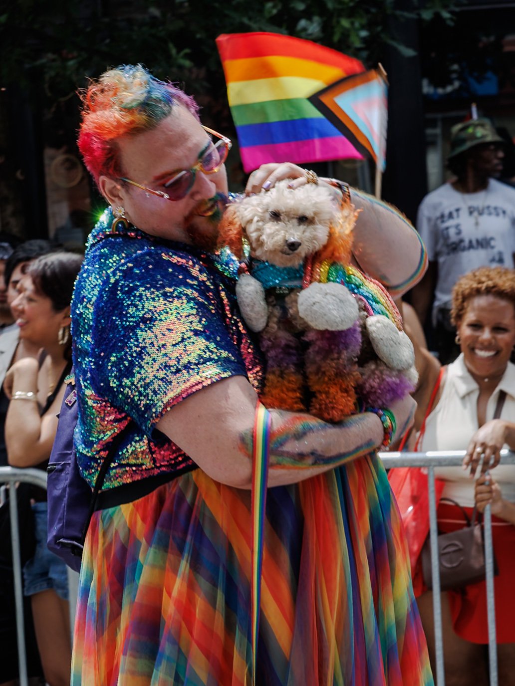 Man holding a small dog in front of a rainbow flag