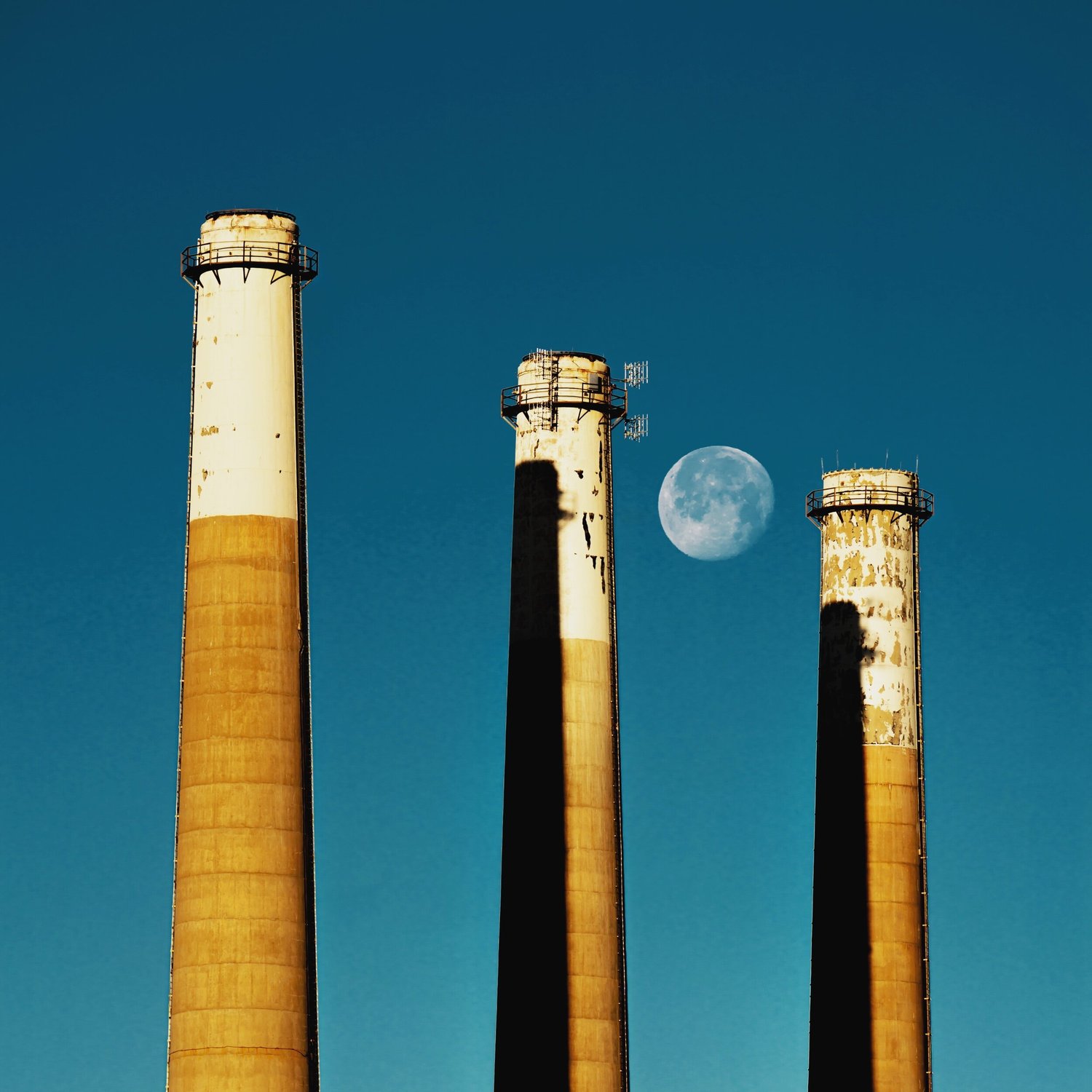 Three smokestacks against a blue evening sky with the moon between them