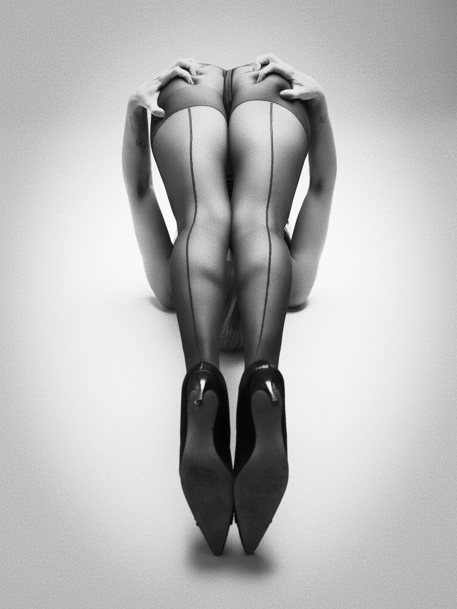 Symmetrical view from behind of a model folded forward on her knees, seamed stockings running down to black heels