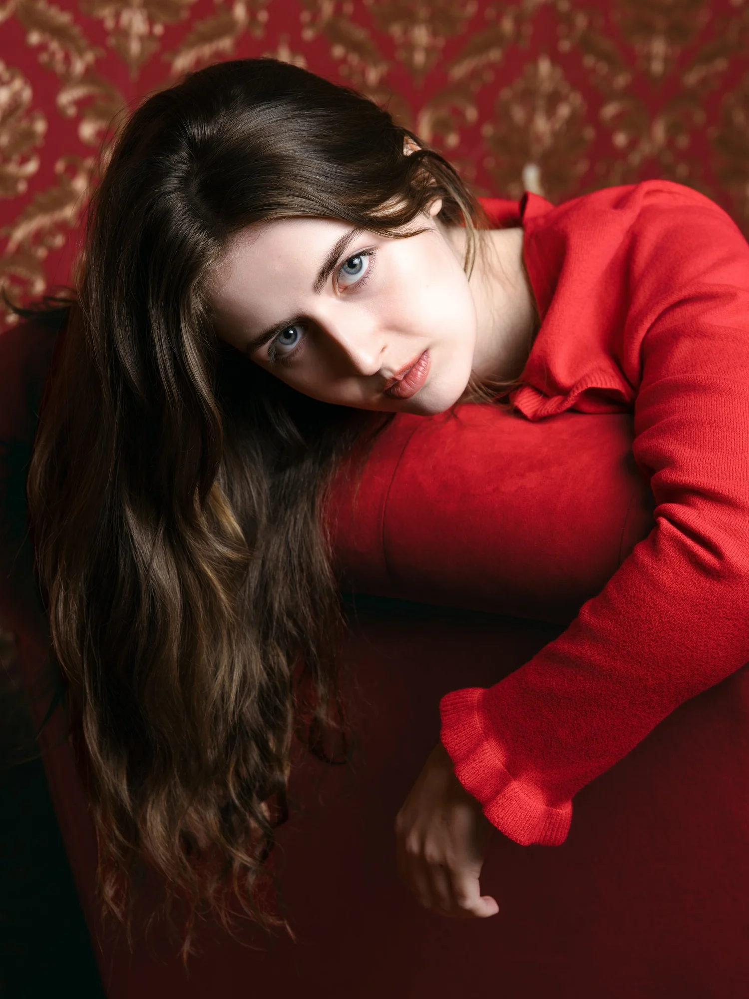 Woman with long dark hair in a red sweater against a red patterned backdrop