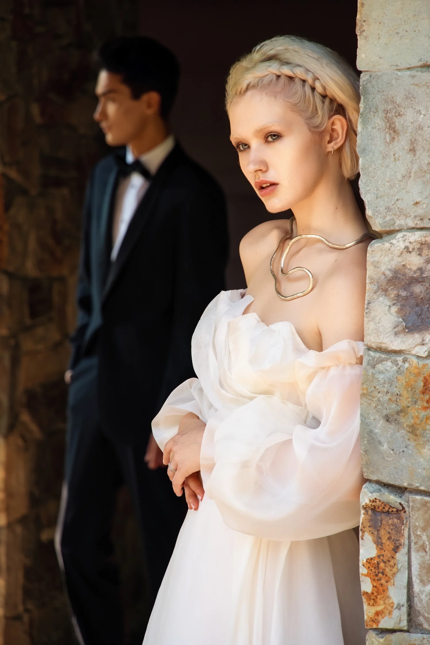 Bride in a white gown and groom in a tuxedo beside a stone wall