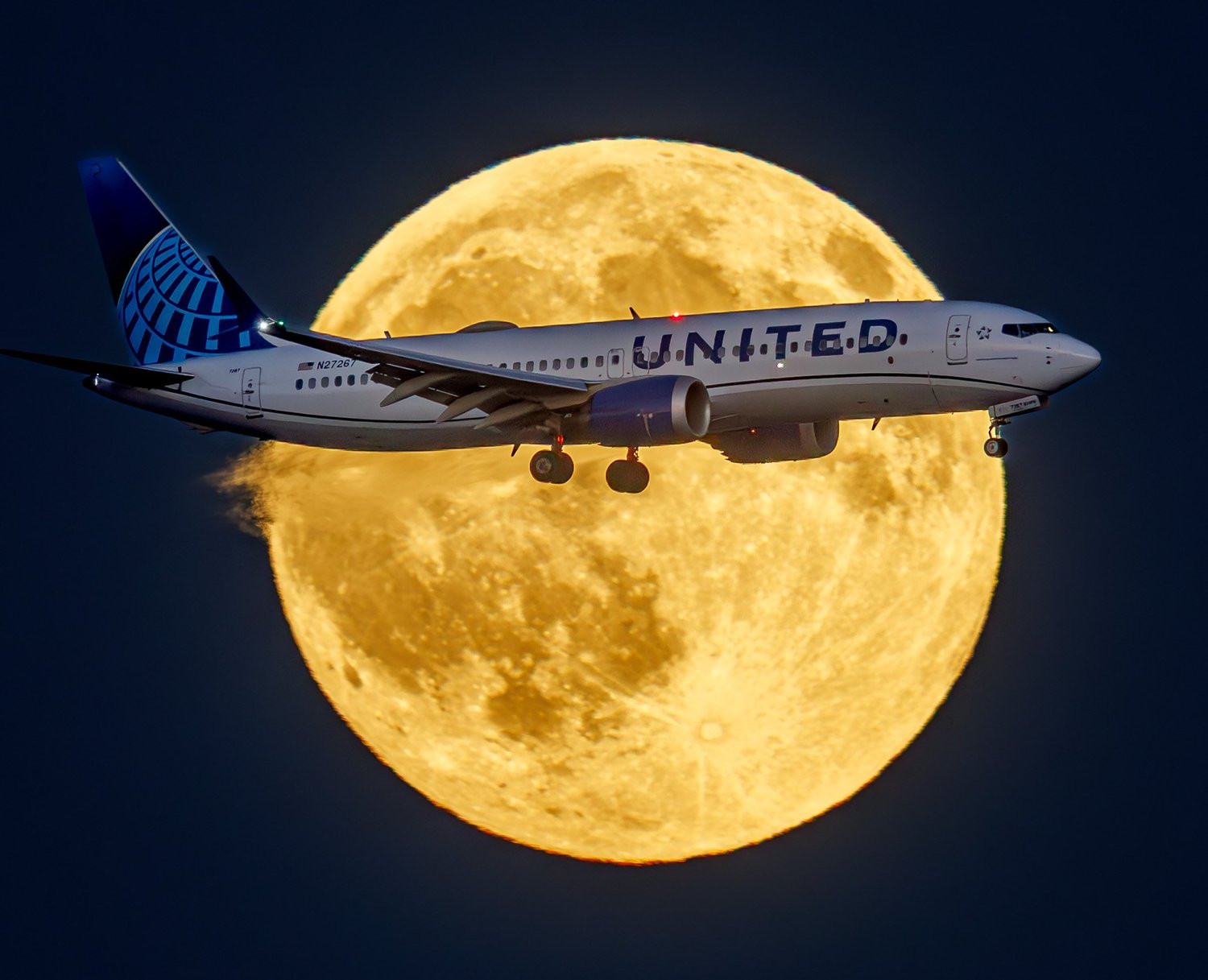 A United Airlines jet crossing in front of a huge full moon