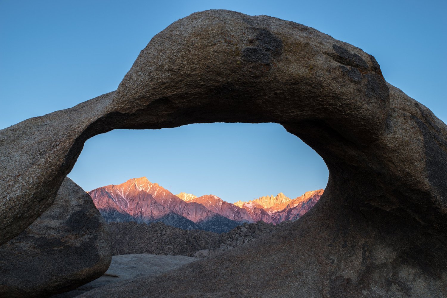 A natural rock arch framing jagged peaks lit pink at sunrise