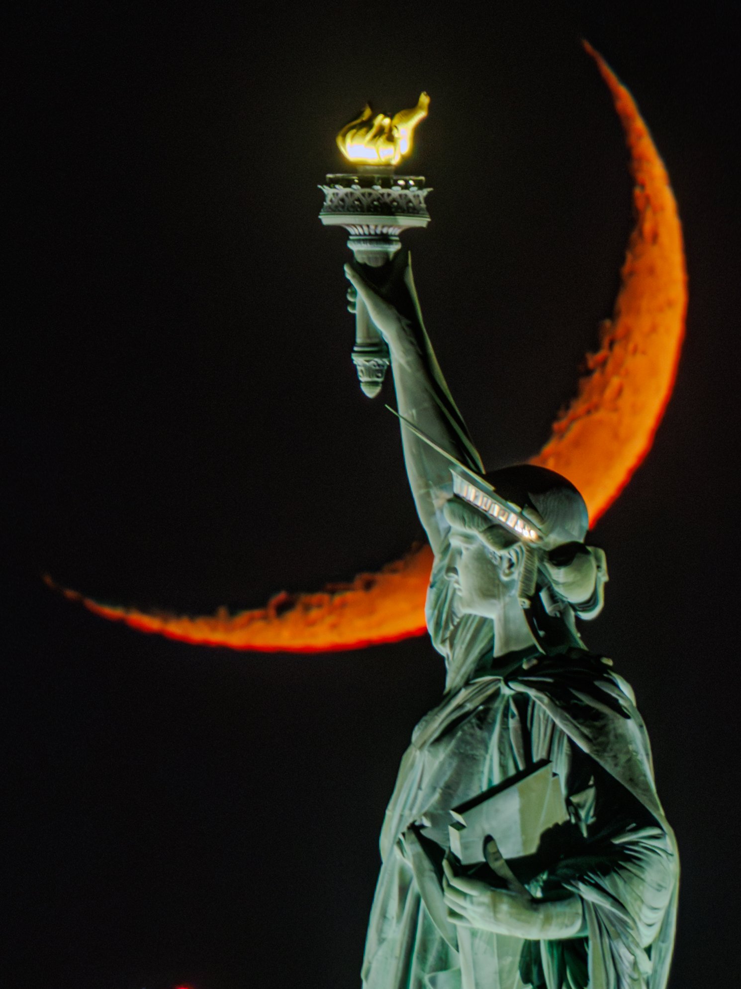 The Statue of Liberty’s torch raised against a thin crescent moon