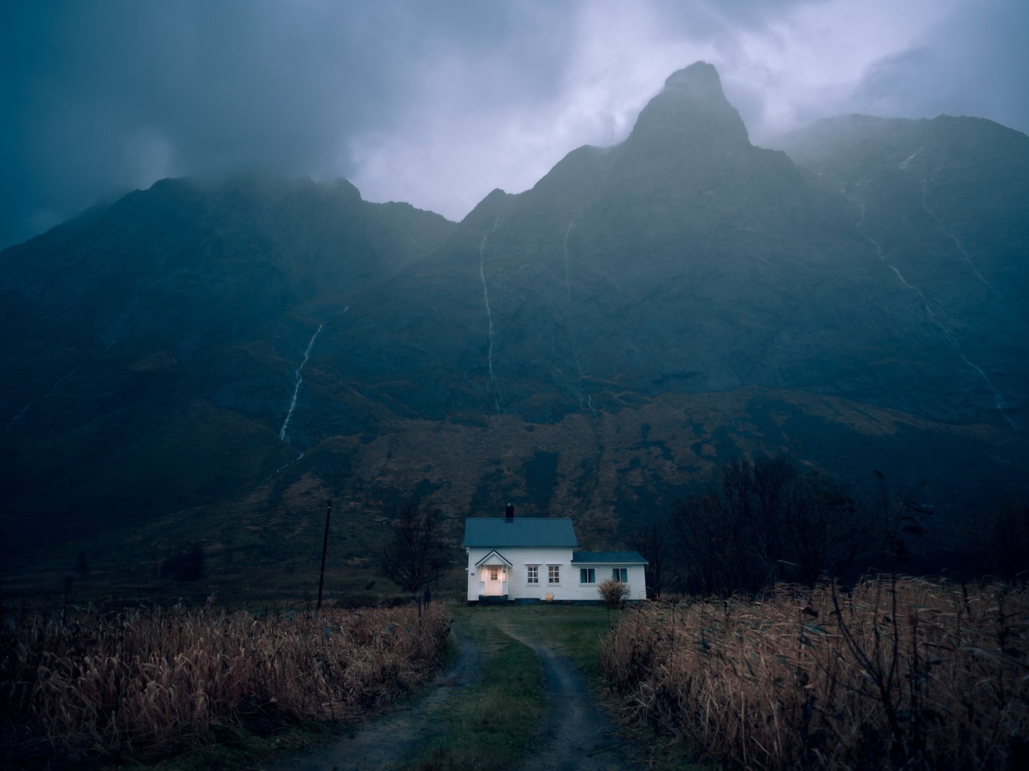 Small white house beneath dark, cloud-wrapped mountains